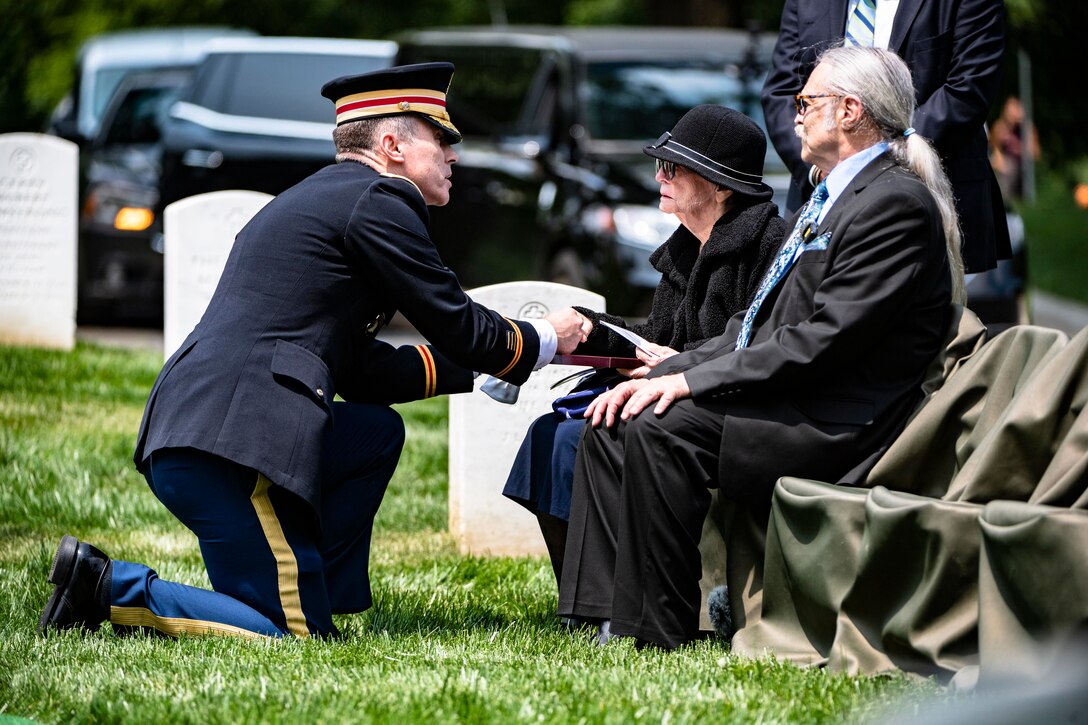 An Army officer kneels and holds a woman's hand during a funeral service.