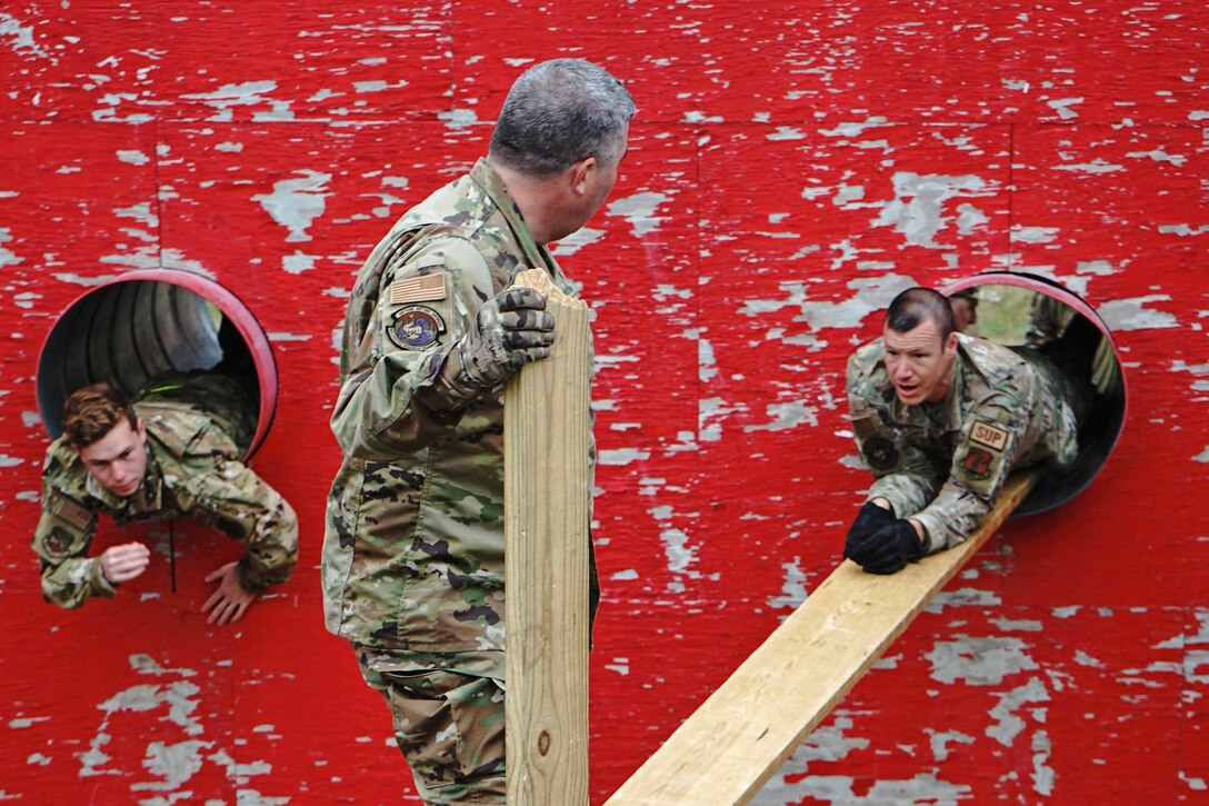 Two airmen climb through holes in a wall while a third watches.