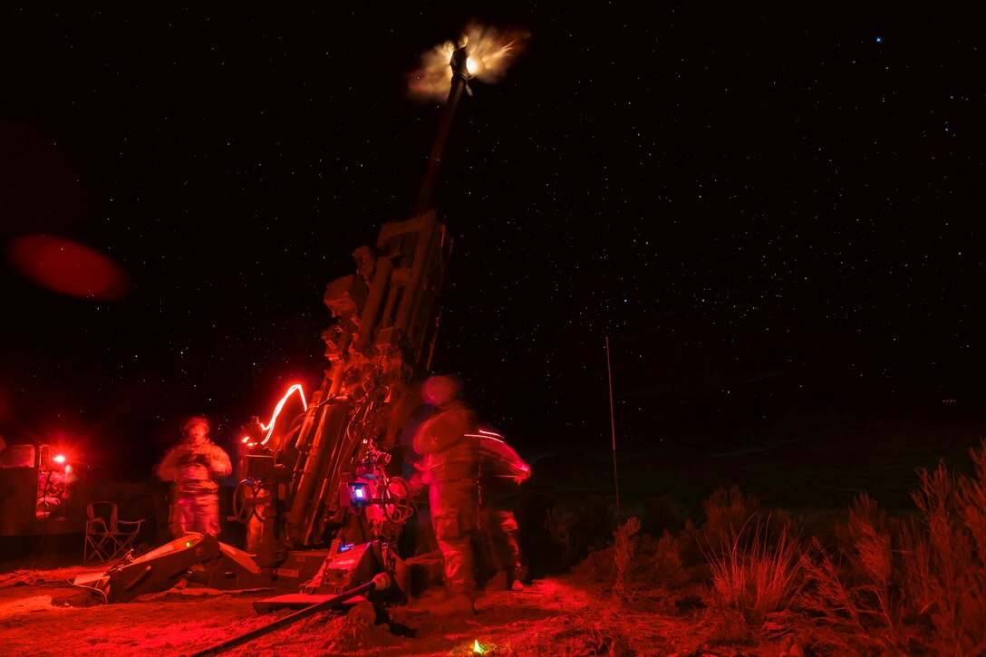 Guardsmen illuminated by red light fire a weapon at night.