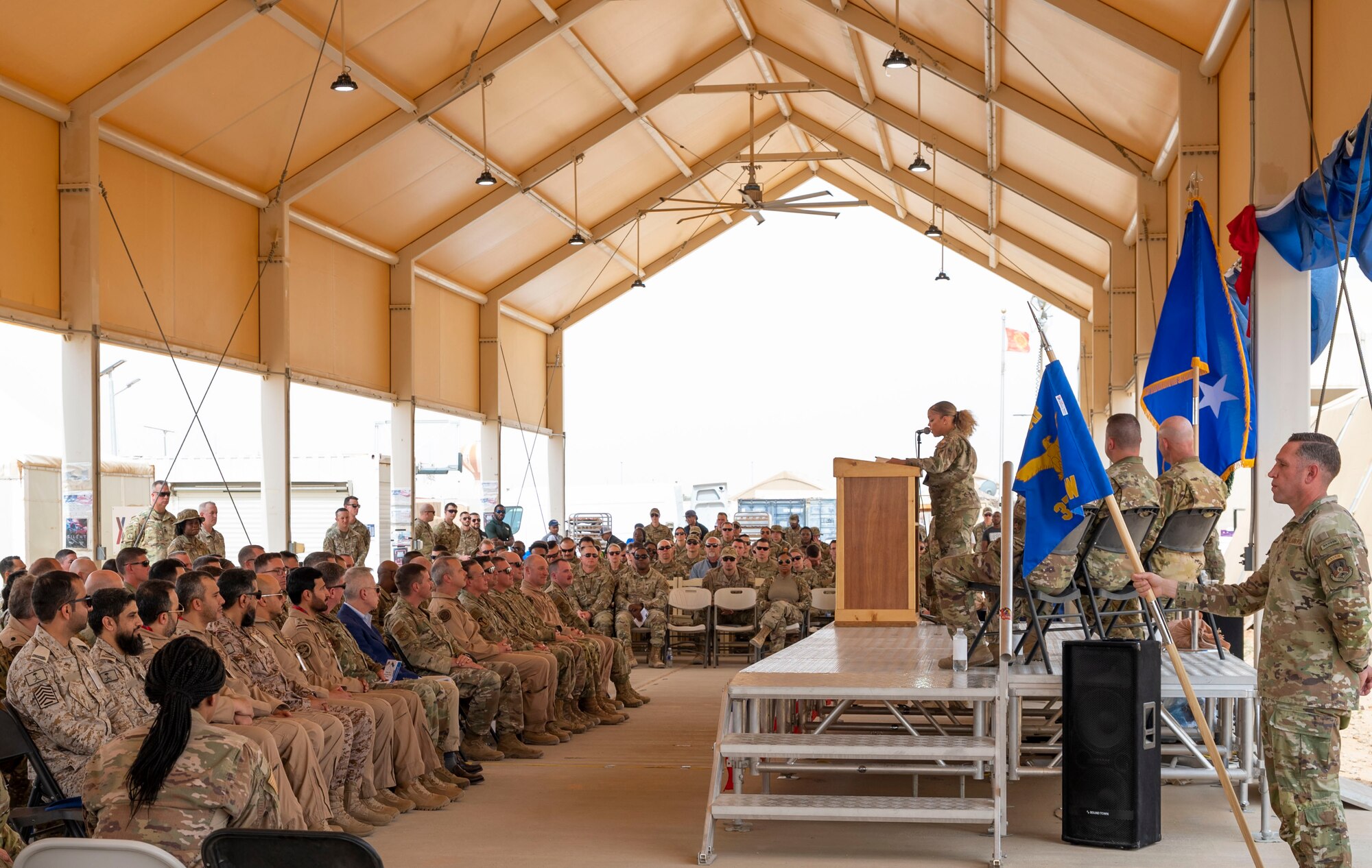 Service members from the Royal Saudi Air Force and 378th Air Expeditionary Wing listen to U.S. Air Force Master Sgt. Sarah Hahn, 378th AEW Equal Opportunity director, narrate during a change of command ceremony at Prince Sultan Air Base, Kingdom of Saudi Arabia, May 18, 2023. During the ceremony, Brig. Gen. William Betts relinquished command of the 378th AEW to Brig. Gen. Akshai Gandhi. The tradition of change of command ceremonies are to allow service members to witness their new leader assume the responsibility and trust associated with the position of commander. (U.S. Air Force photo by Senior Airman Stephani Barge)