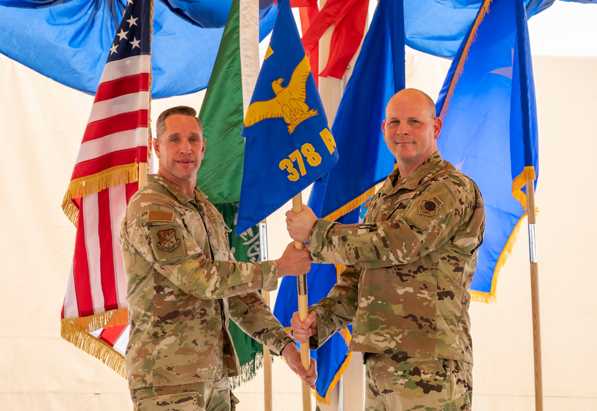 U.S. Air Force Chief Master Sgt. William Kelly, left, outgoing 378th Air Expeditionary Wing command chief, passes the guidon to Chief Master Sgt. Randolph Crosslin, incoming 378th AEW command chief, during a change of command ceremony at Prince Sultan Air Base, Kingdom of Saudi Arabia, May 18, 2023. During the ceremony, Brig. Gen. William Betts relinquished command of the 378th AEW to Brig. Gen. Akshai Gandhi. The tradition of change of command ceremonies are to allow service members to witness their new leader assume the responsibility and trust associated with the position of commander. (U.S. Air Force photo by Senior Airman Stephani Barge)