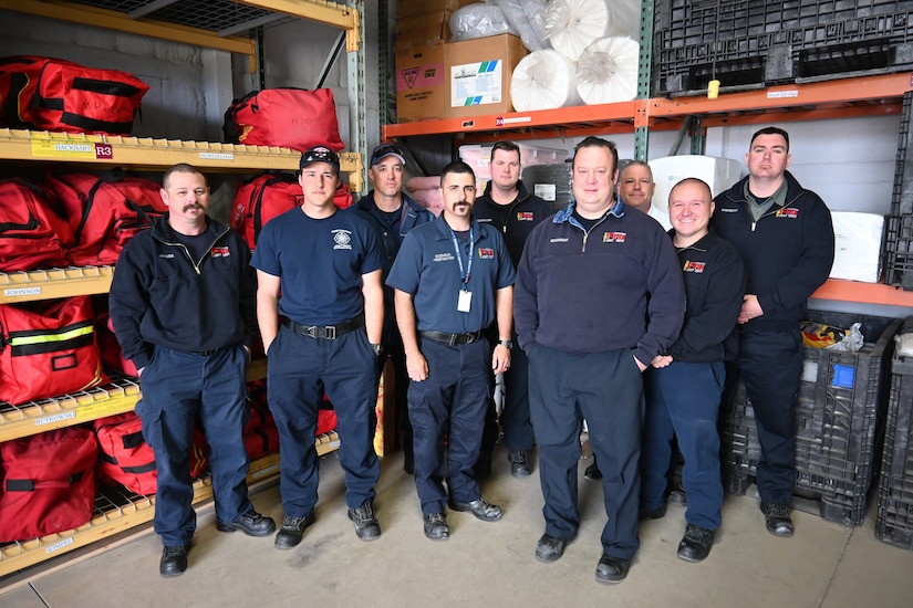 Photo of Fire and Emergency Services Branch members standing in firehouse storage area.