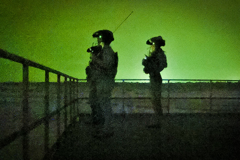 Airmen look into the distance at night, illuminated by a green light.