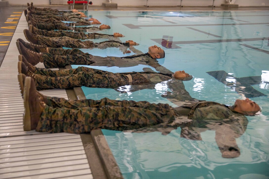 Marine Corps recruits float with their feet on the side of the pool.