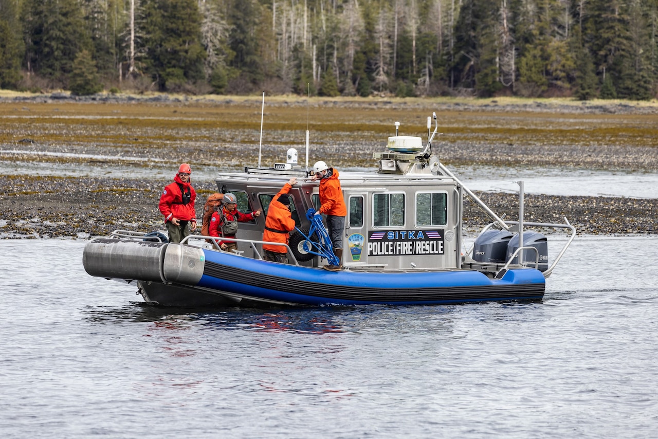 People wearing hard hats work aboard a small boat in water.