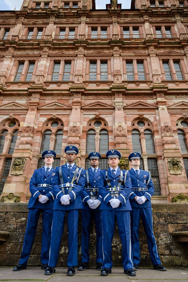 Six uniformed members of an honor guard pose with their backs to a castle wall.