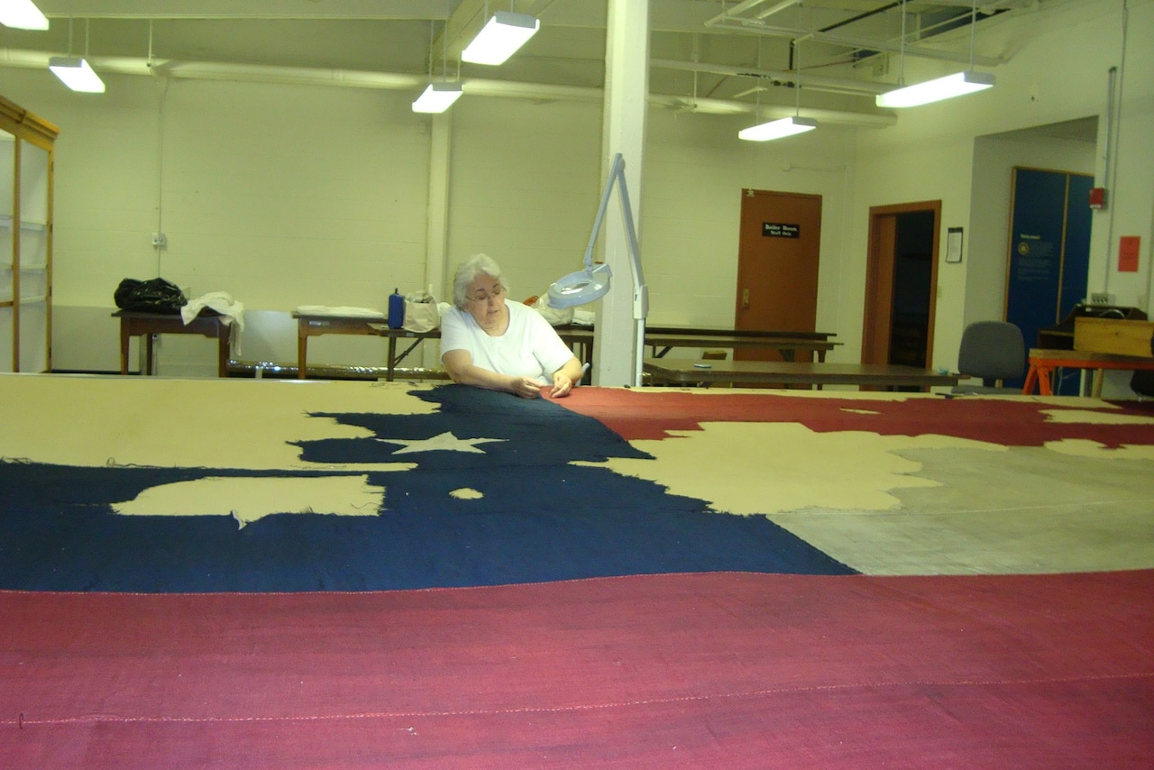 A woman sits at a table surrounded by a huge flag.
