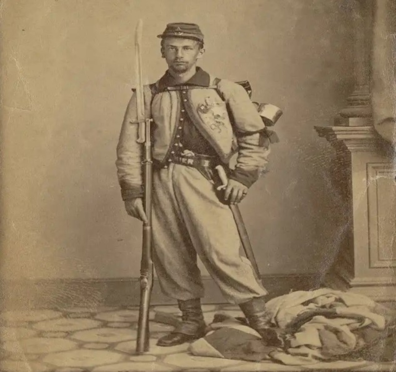 A man wearing a uniform stands while holding a rifle with bayonet.