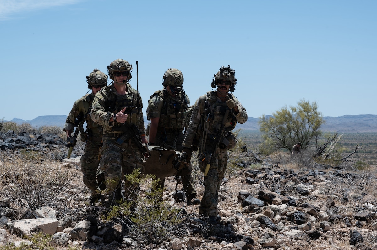 U.S. Air Force pararescuemen carry a simulated downed pilot toward a HH-60W Jolly Green II helicopter in Arizona, May 13, 2023. The pararescuemen signaled to confirm permission to board the helicopter. (U.S. Air Force photo by Airman 1st Class Jasmyne Bridgers-Matos)
