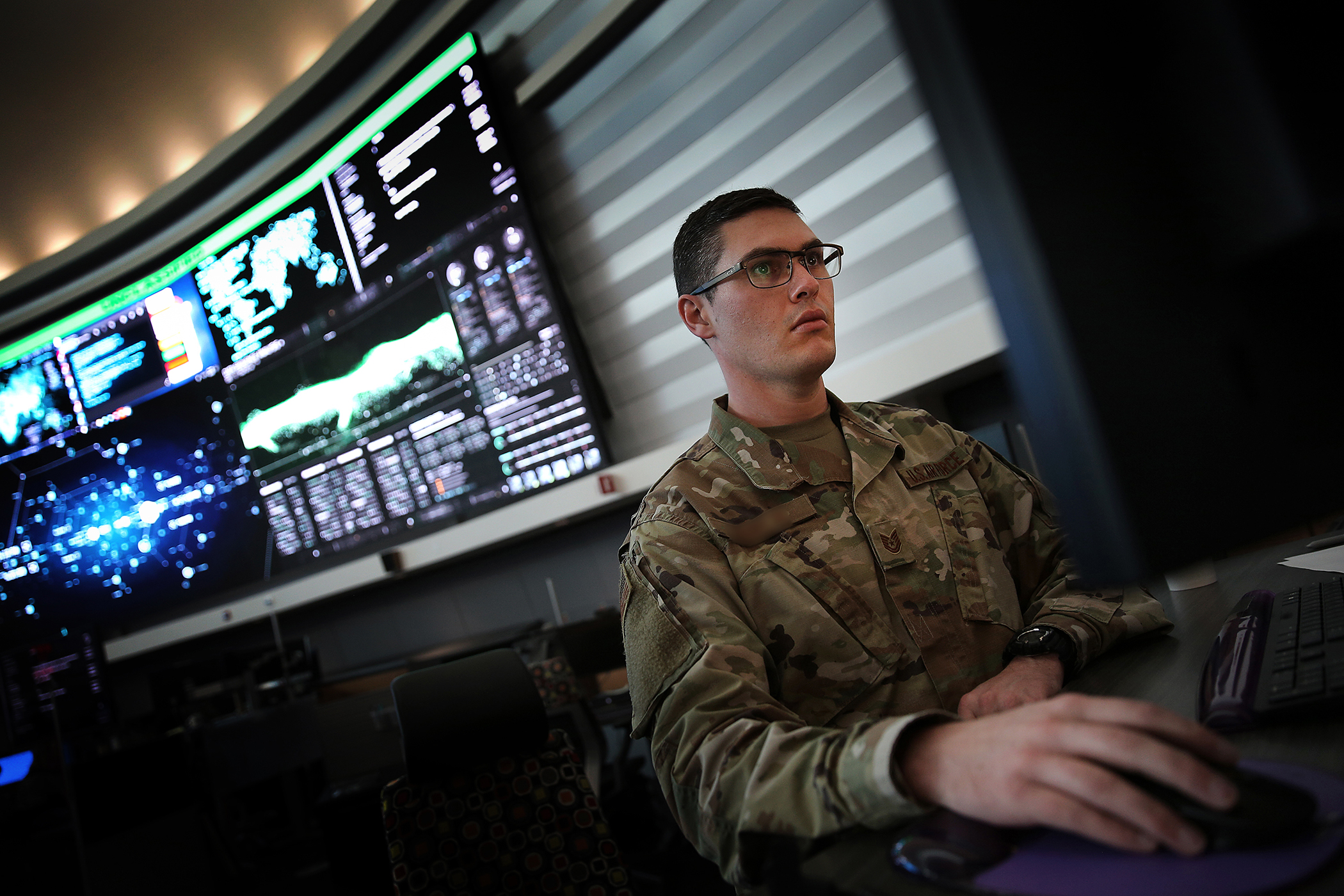 A soldier sits at a table and looks at a laptop screen with his hands on the keyboard.