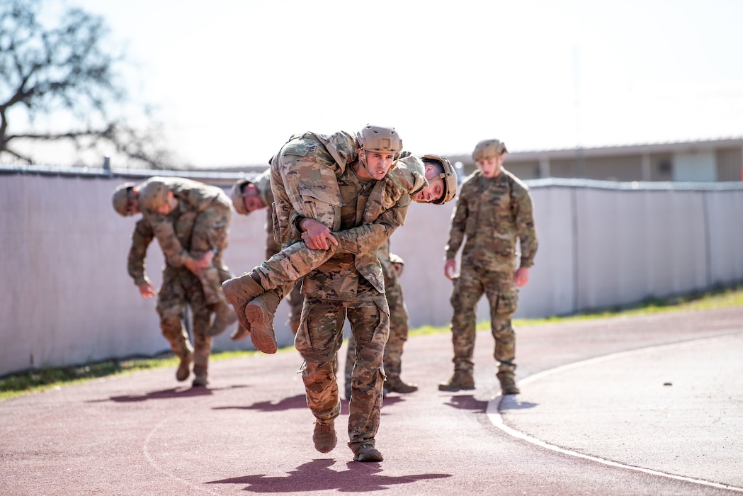 Airmen carry each other around a track in the bright sunlight