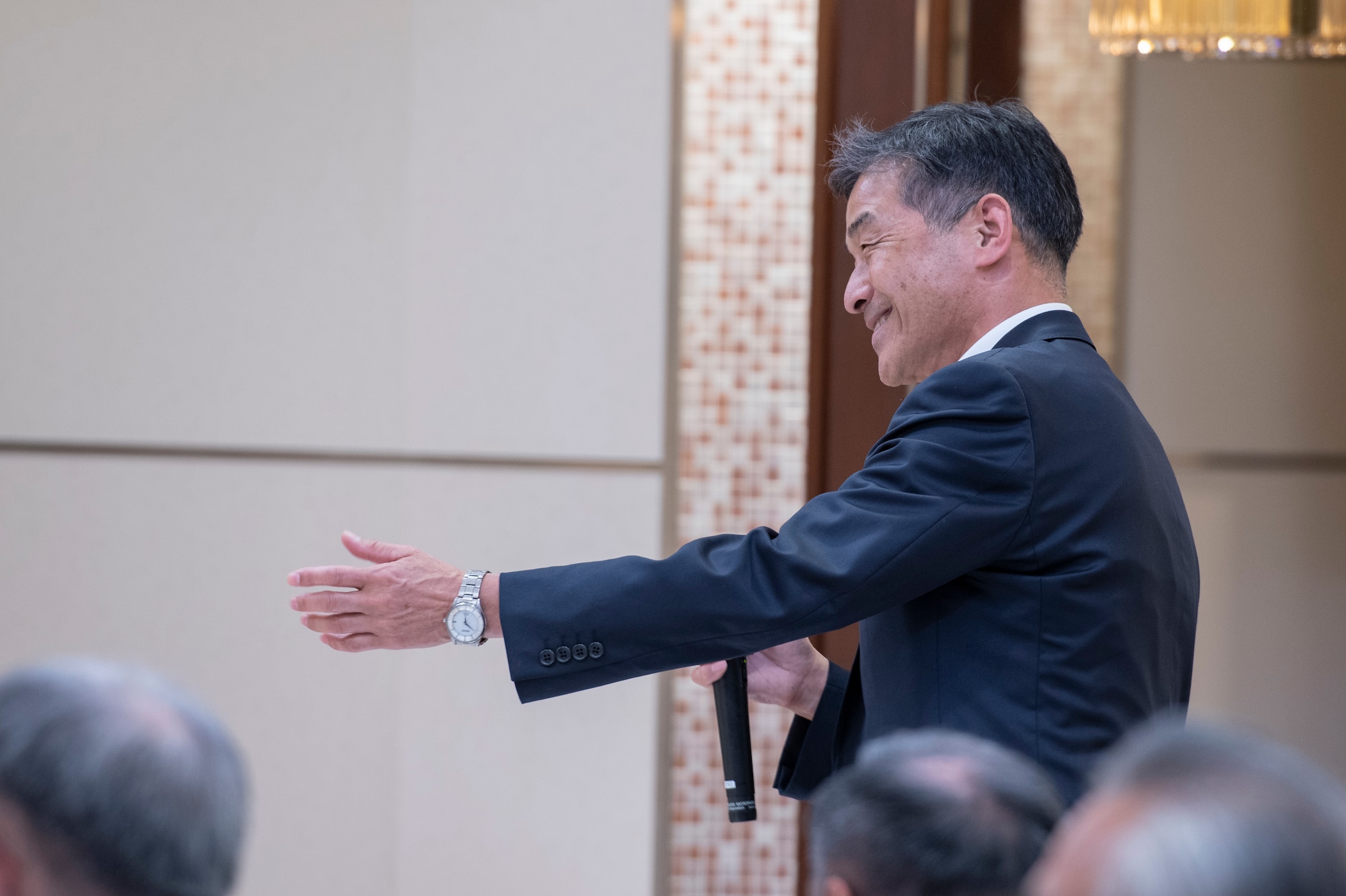 A Japanese man in a suit gestures to a speaker