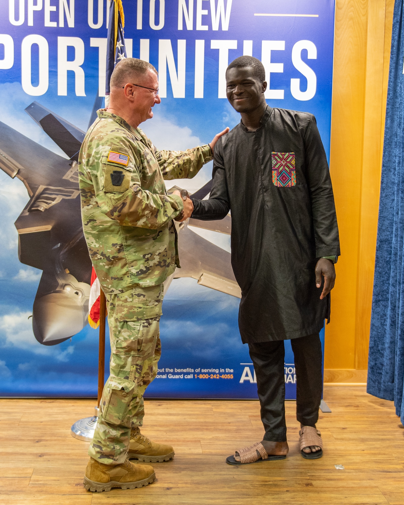 The newest member of the 158th Fighter Wing, Airman Libass Mbengue, shakes hands with Maj. Gen. Gregory Knight, adjutant general of the Vermont National Guard, at Vermont Air National Guard Base, South Burlington, Vermont, May 18, 2023. Mbengue moved to Vermont in 2018 from Senegal, Africa.