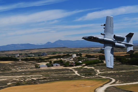 A plane flies low across a rural landscape.