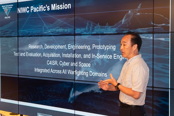 Photo of Eric Inouye giving a brief in front of a digital wall.