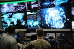 A man standing next to another man in uniform points to a large watch floor display.