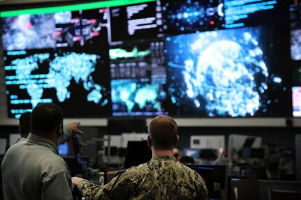 A man standing next to another man in uniform points to a large watch floor display.
