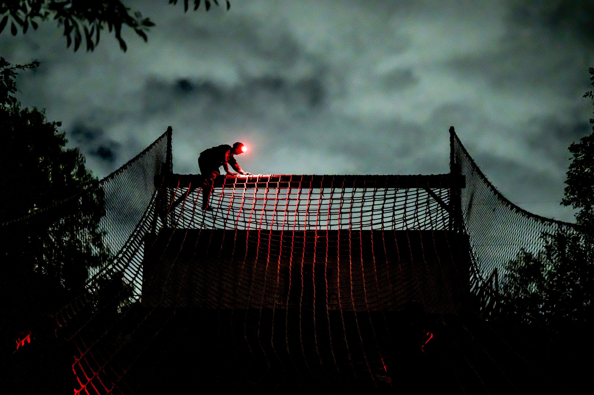 candidate sits on top of rope wall in the dark while his red headlamp illuminates the ropes