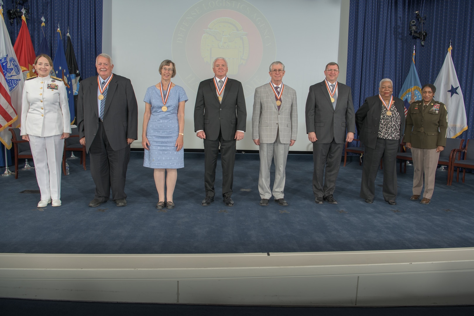 The six new members of DLA's Hall of Fame stand on a stage with the agency's director and senior enlisted leader.