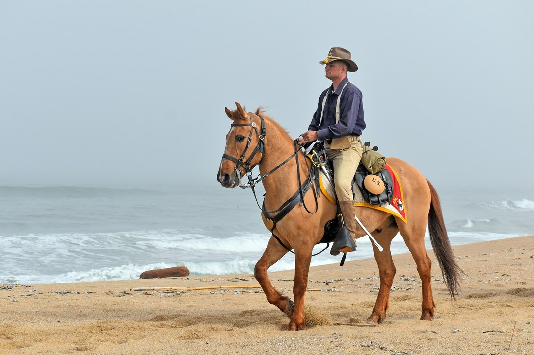 A service member rides a horse on the beach.