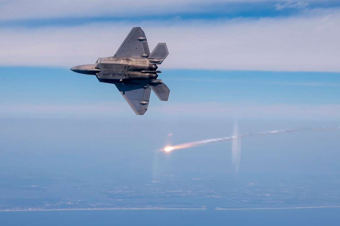 An aircraft flies on its side parallel to a flare over a body of water.