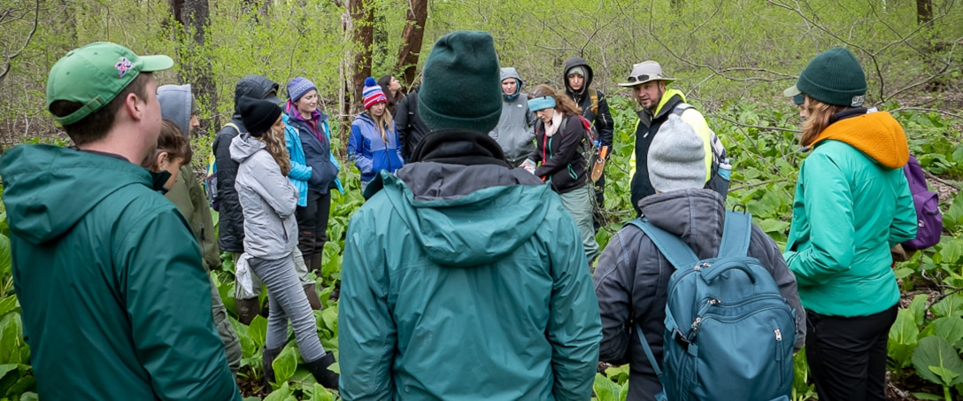 A group of people dressed warmly and protected from the elements, gathered in a heavily wooded and vegetated area near Kent State University in Kent, Ohio.