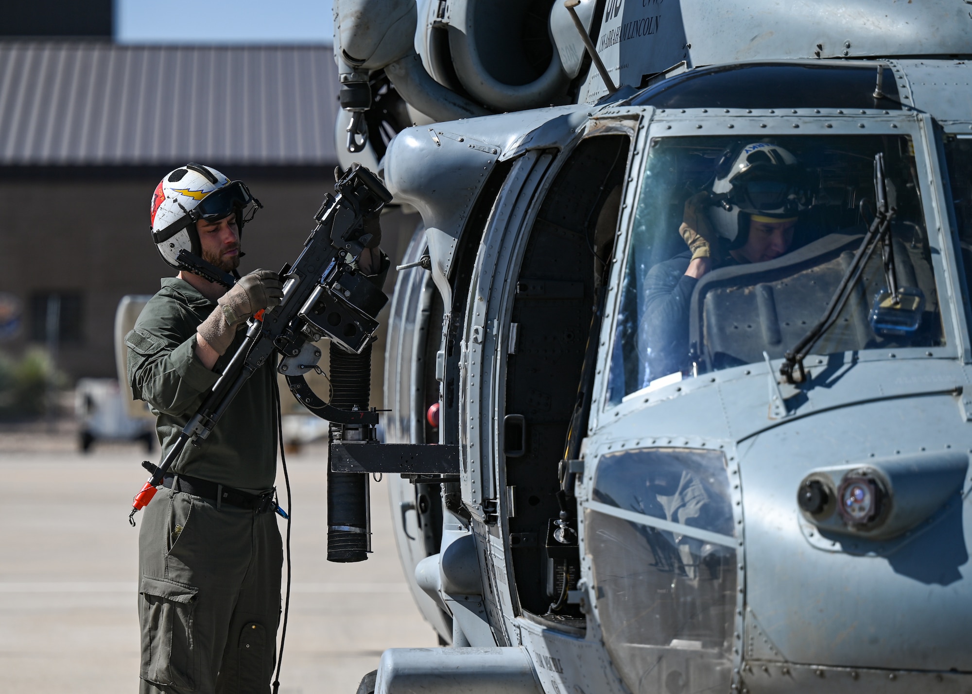 A man in a military uniform inspects a weapon attached to a helicopter.