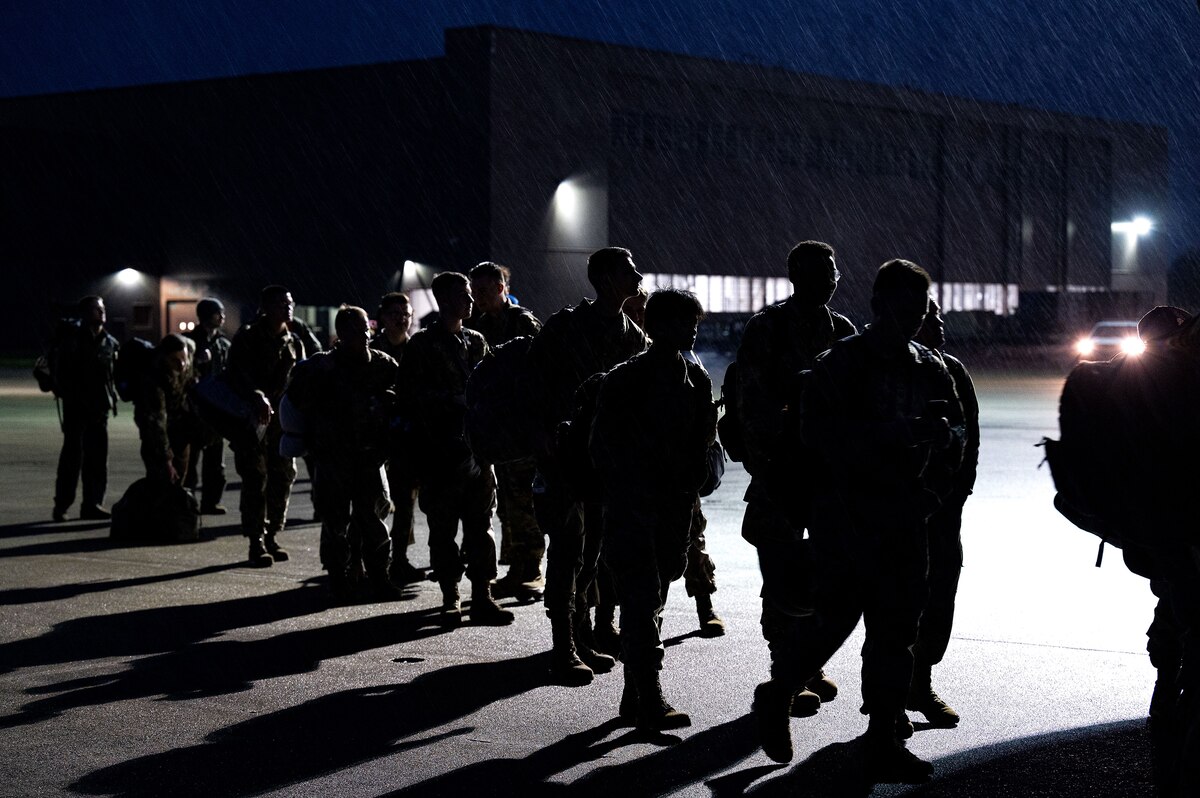 Airmen shown in silhouette walk on a dark flight line.