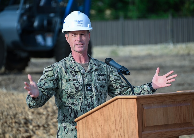A man in a uniform with a hard hat speaks at a lectern.