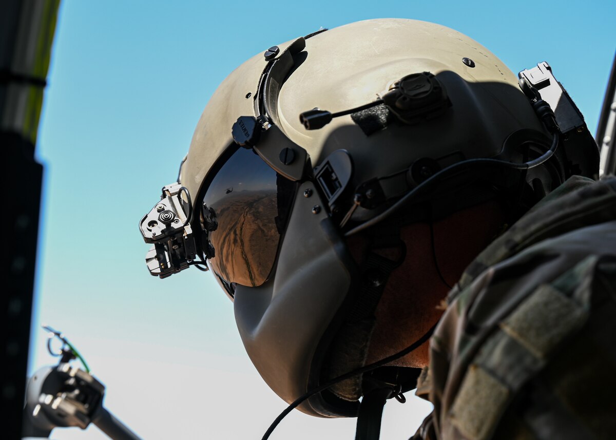 A man in a military uniform looks out the window of a helicopter.