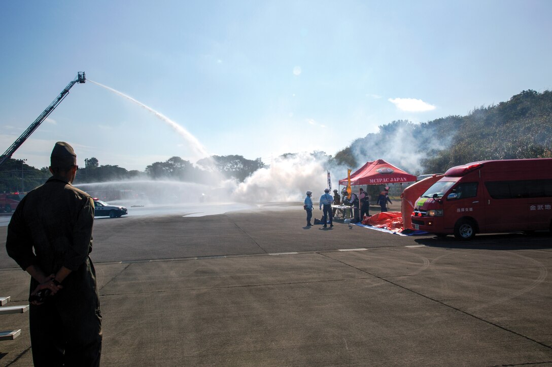 While firefighters respond to a simulated aircraft fire in the back, a joint command center is set up, to the right, for initial tasking to assist in the emergency response during the joint training exercise for a simulated air accident.