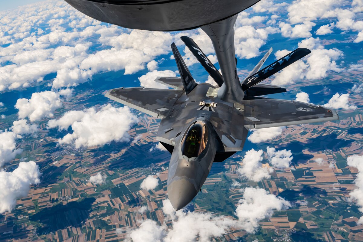 An Air Force jet flies beneath the boom of a tanker aircraft in a cloud-speckled sky.