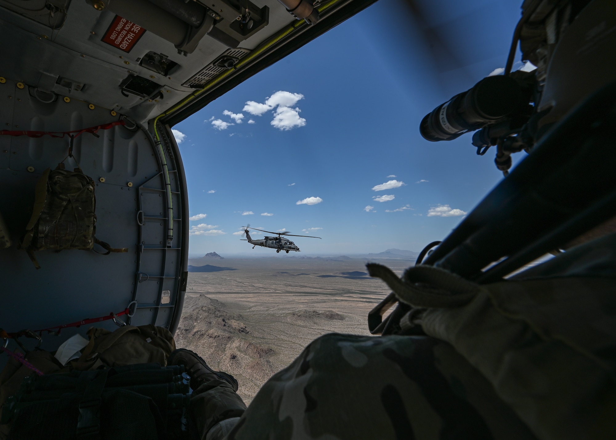 A man in a military watches a helicopter fly over the desert.