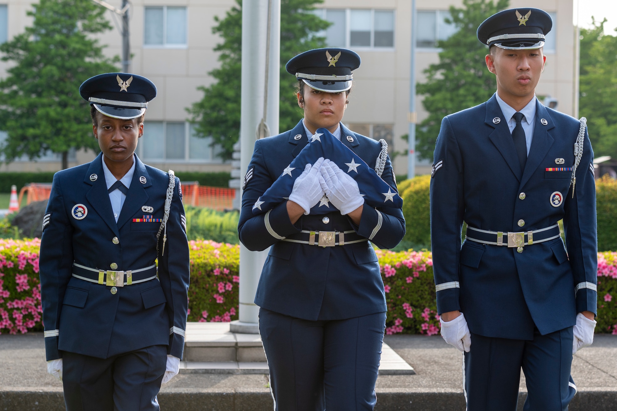 three formal uniform clad people hold a US flag