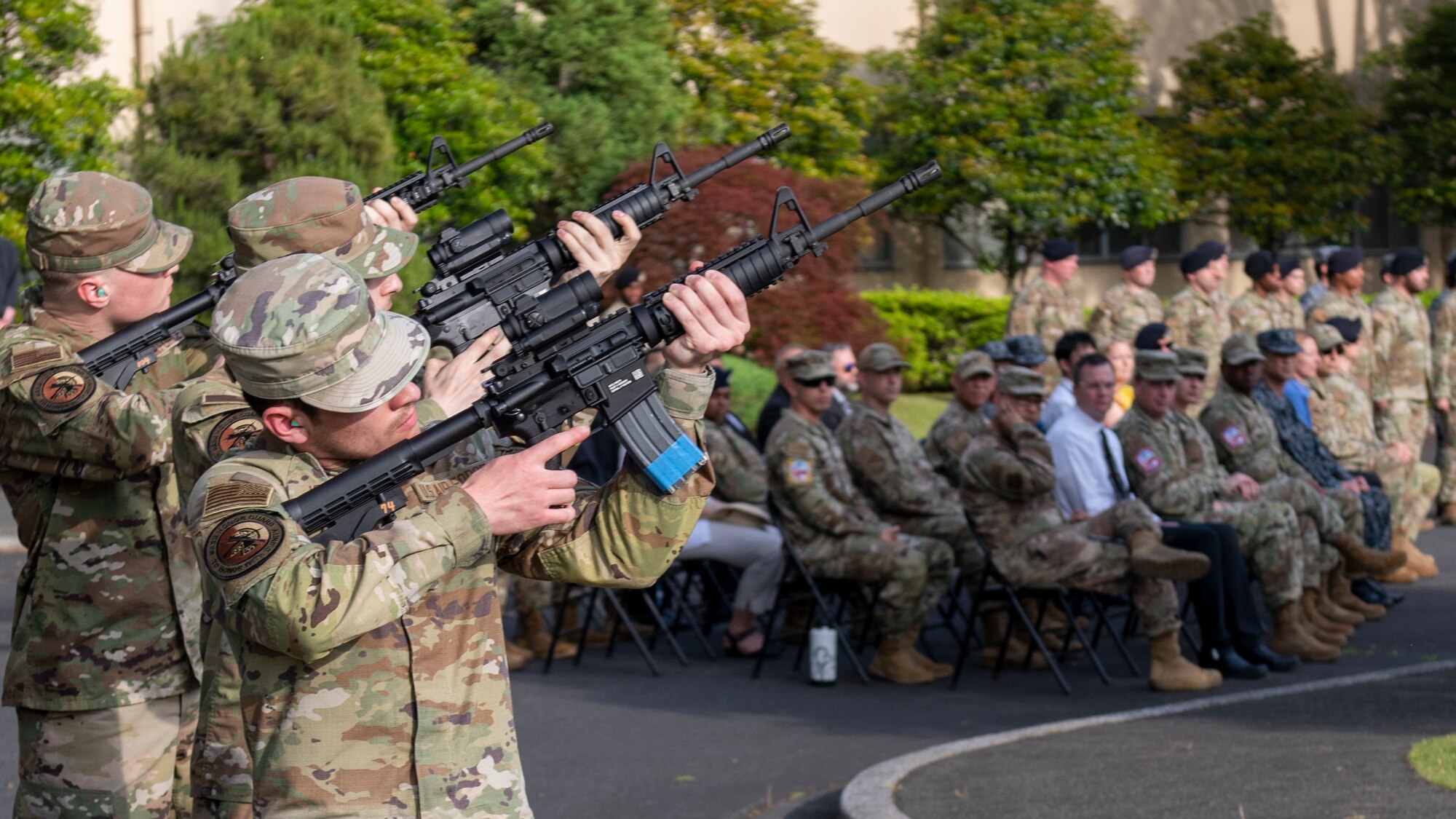 a crowd watches three soldiers fire rifles into the air