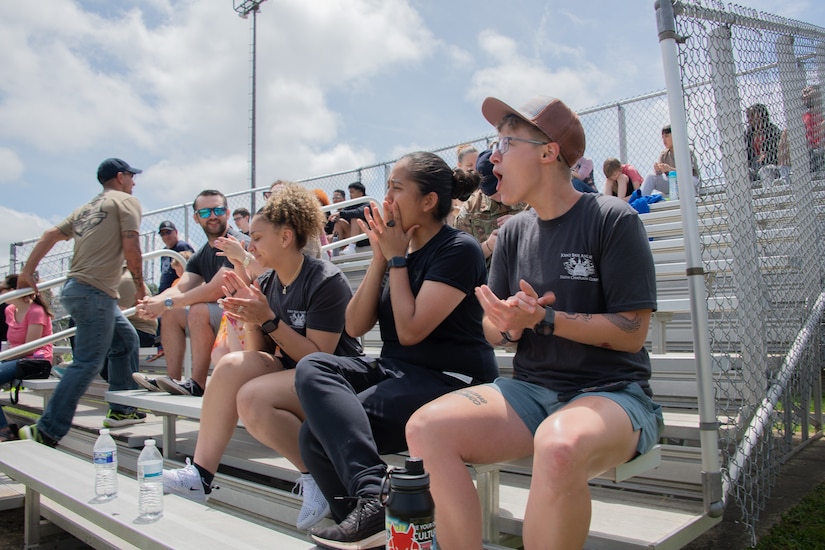 A crowd cheers while sitting on bleachers.