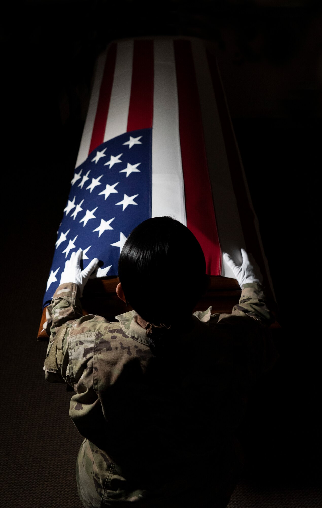 An Airman stands over a casket with a flag over it.