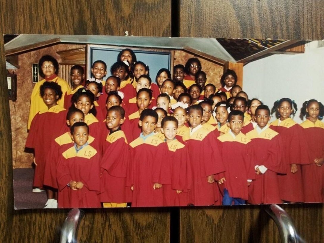 A older photo of a group of children in red and gold choir robes poses inside of a church.