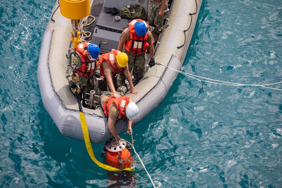 Sailors pull a mock torpedo out of the water.