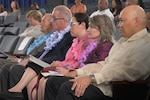 Two men and one woman sit on a stage facing one another