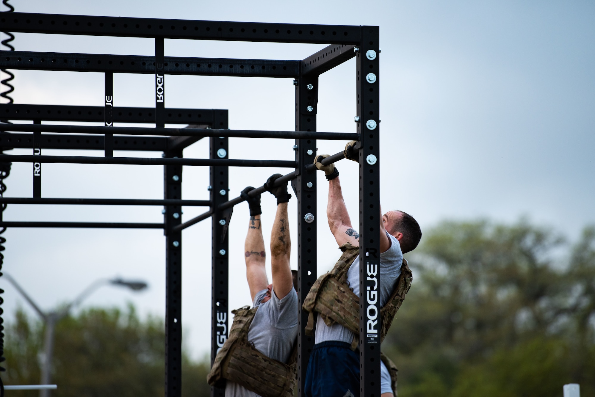 Airmen complete pullups on an outdoor bar as the sun rises