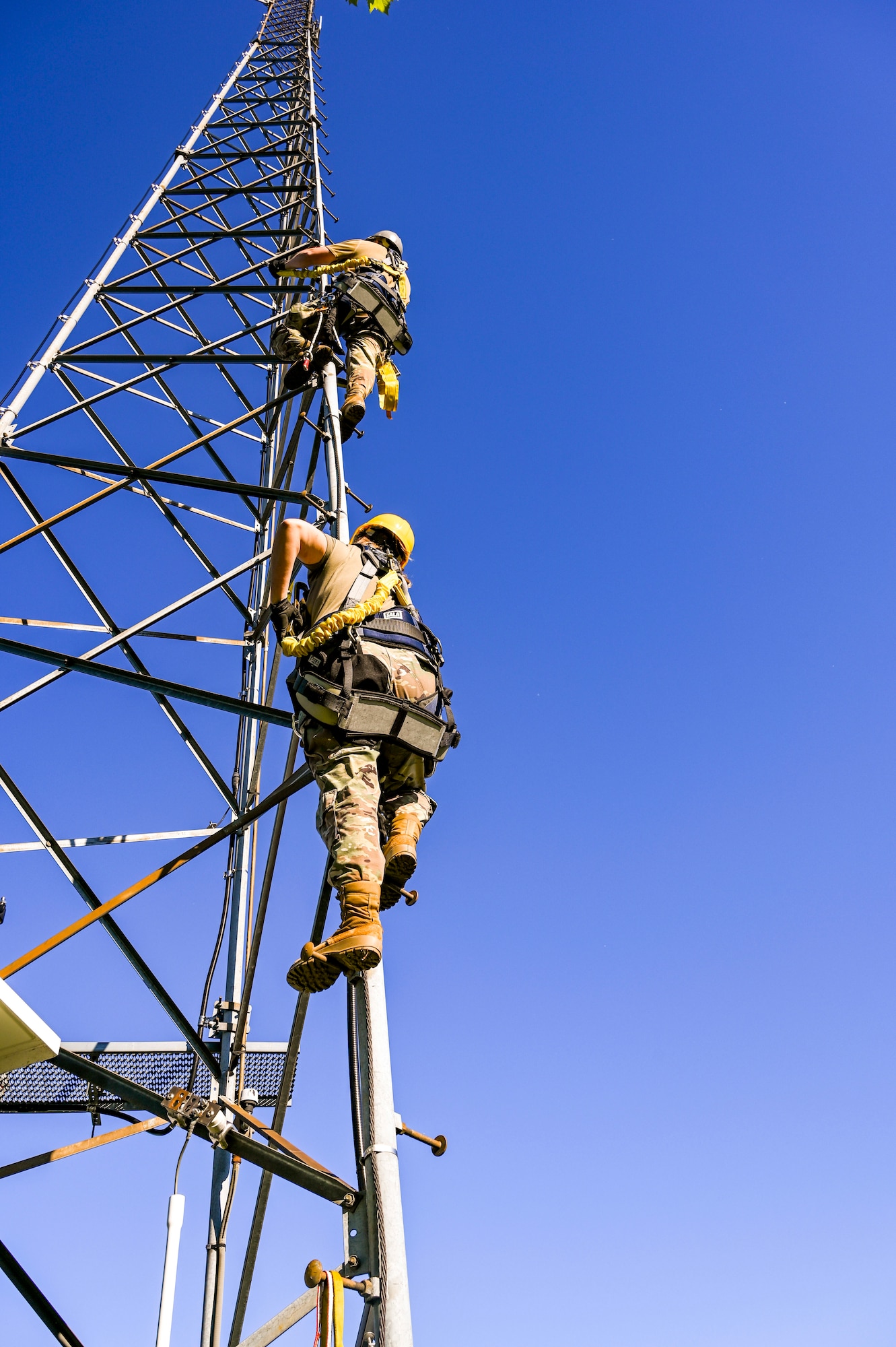 People wearing hard hats and harnesses climb a metal structure.