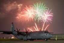 An aircraft sits on a flight line with a firework display in the background.