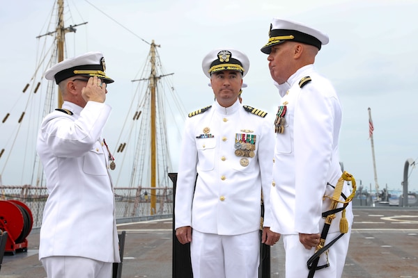 Capt. Brian Hogan, commodore, Submarine Squadron Eight, center, observes Cmdr. Chris Turner, right, relieve Cmdr. Ryan Heineman, left, as commanding officer of the Virginia-class attack submarine USS John Warner (SSN 785) during a change of command ceremony aboard the decommissioned Iowa-class battleship USS Wisconsin.