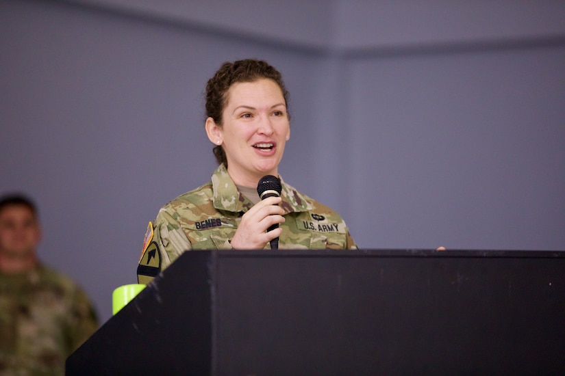 Lt. Col. Tenay Benes faces forward and addresses Soldiers. She holds a microphone in her hands.