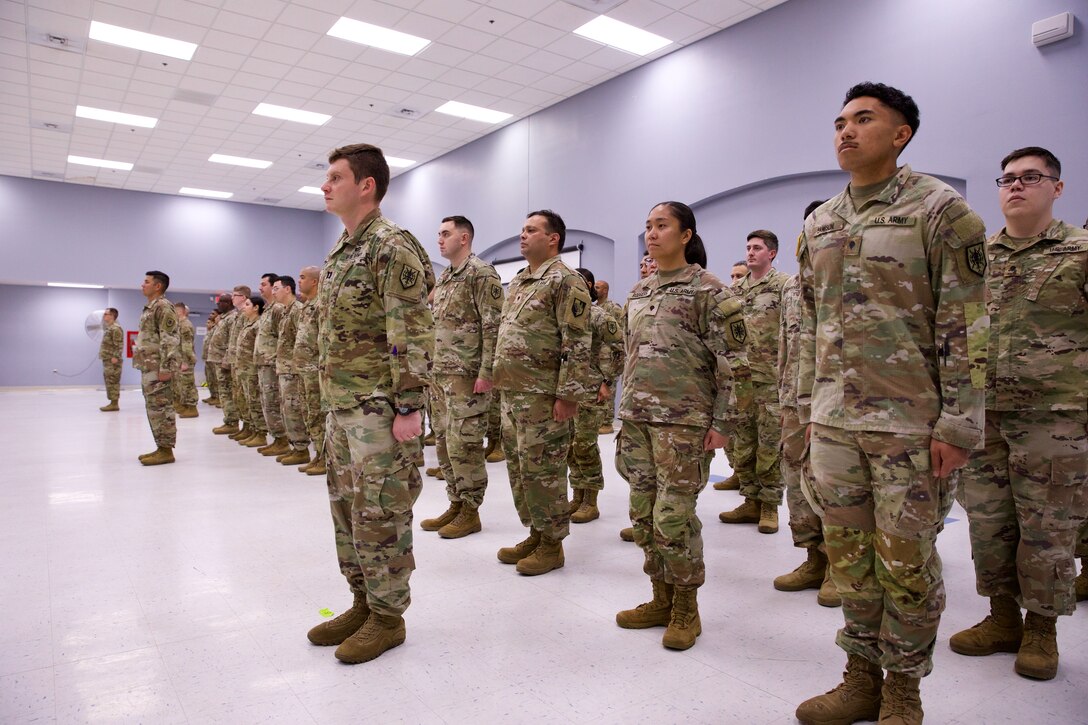 Approximately 100 Soldiers stand at attention, facing forward. They are arranged in a neat formation, with their officers standing to their front.