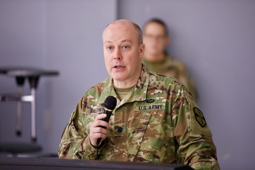 Lt. Col. Clay Baldwin, a Soldier, stands at a podium and addresses the audience using a microphone.