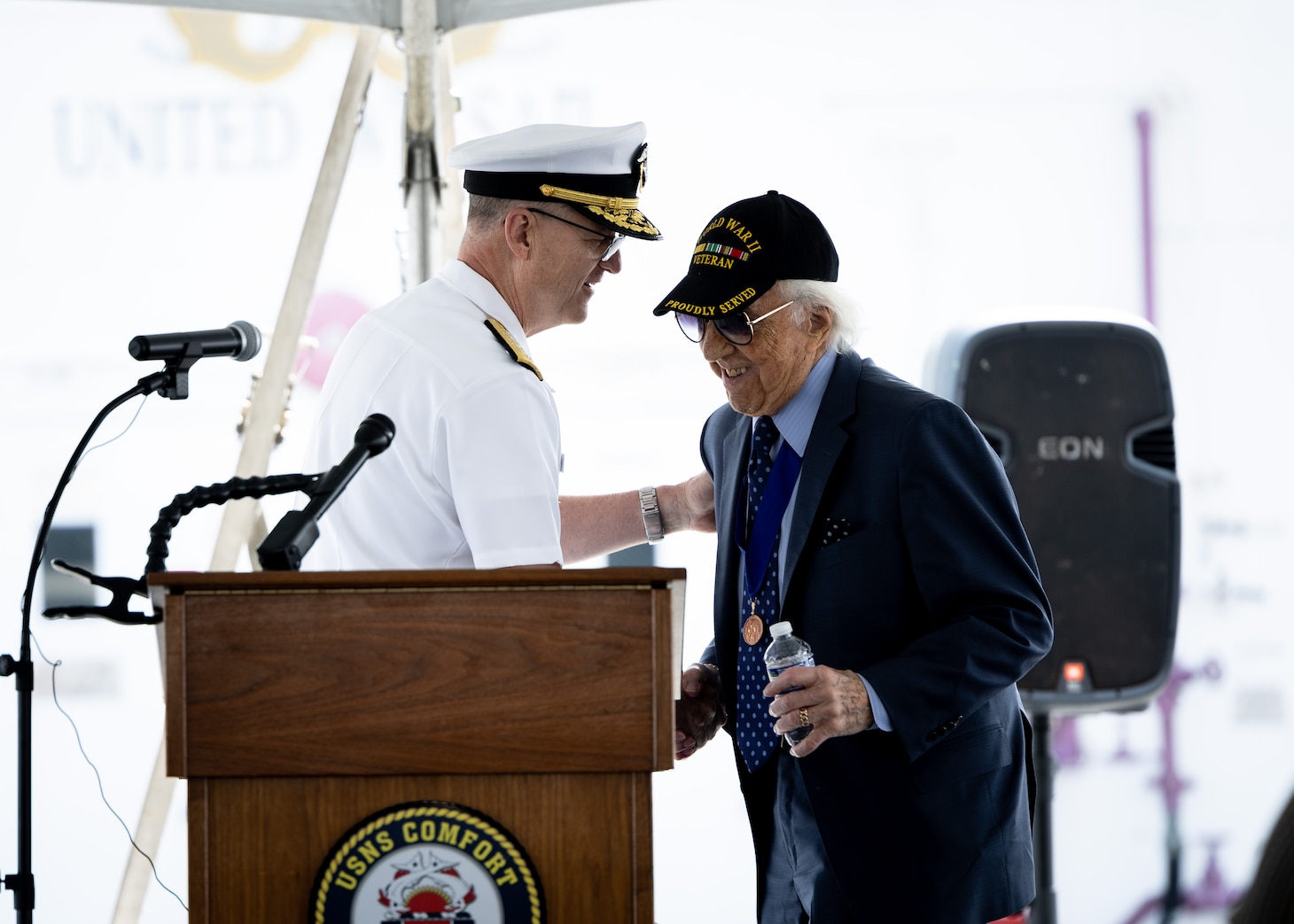 Dave Yoho, U.S. Merchant Marine and World War II Veteran, is greeted at the podium by Rear Adm. Michael Wettlaufer, USN Commander, Military Sealift Command (MSC), during MSC’s National Maritime Day ceremony aboard USNS Comfort (T-AH 20) May 22, 2023. National Maritime Day honors the thousands of dedicated merchant mariners who served aboard United States vessels around the world.