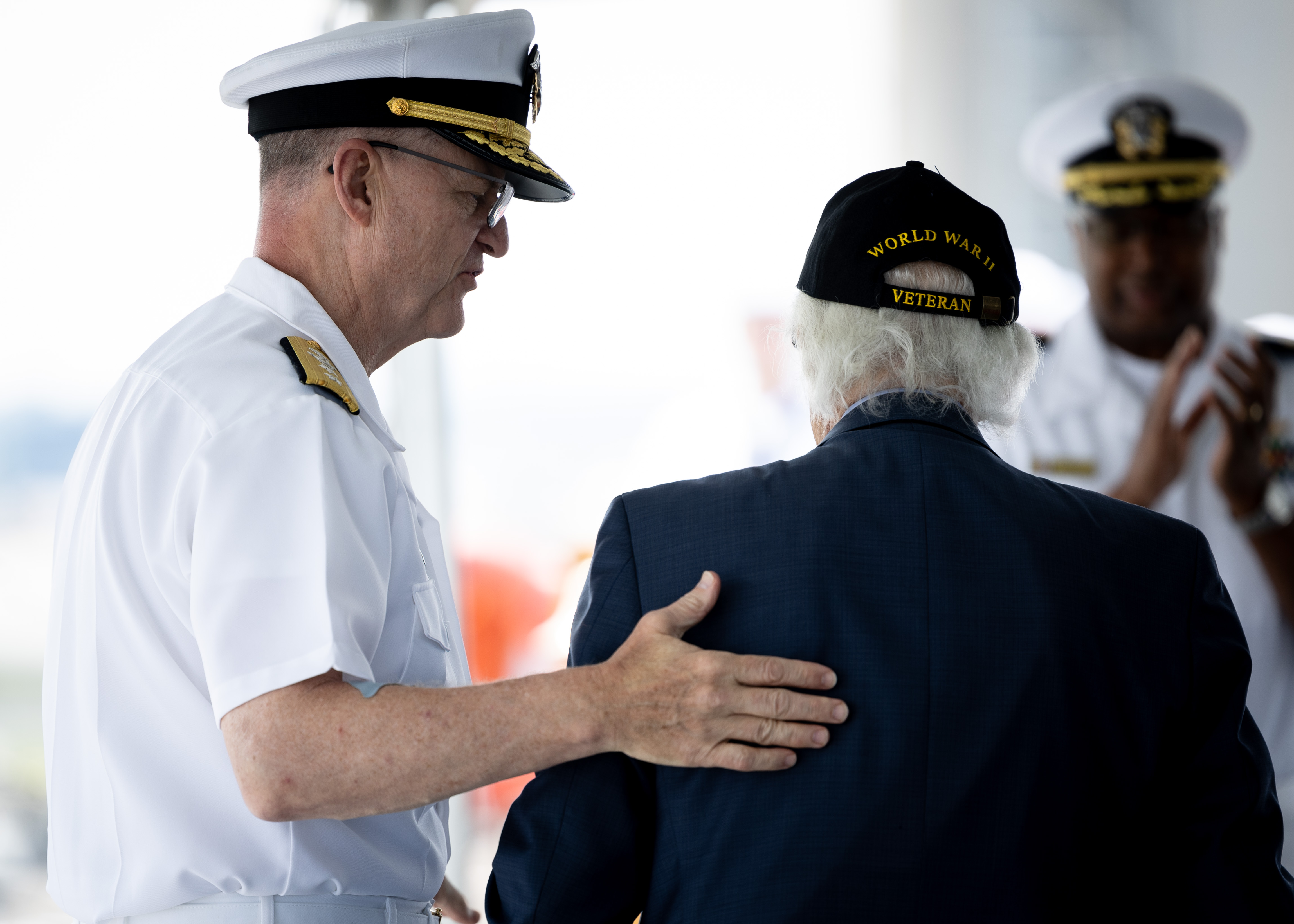 Rear Adm. Michael Wettlaufer, USN Commander, Military Sealift Command (MSC), walks Dave Yoho, U.S. Merchant Marine and World War II Veteran, back to his seat during MSC’s National Maritime Day ceremony aboard USNS Comfort (T-AH 20) May 22, 2023. National Maritime Day honors the thousands of dedicated merchant mariners who served aboard United States vessels around the world.