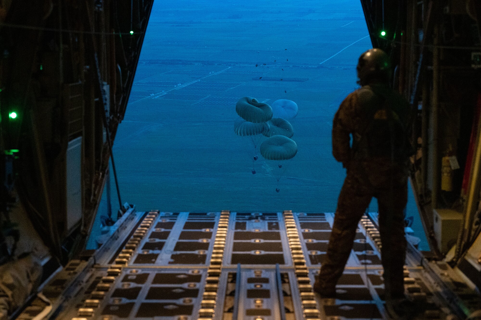a person stands on the ramp watching cargo parachute down to the grounde